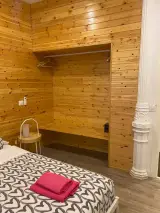 Nicho abierto de madera con barra y perchas en la habitación, con la cama, toallas rosas y una mesita redonda